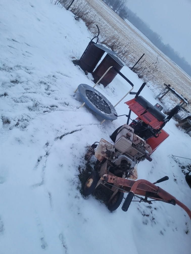 Snow-covered yard with two orange machines and a tire beside a metal bin.