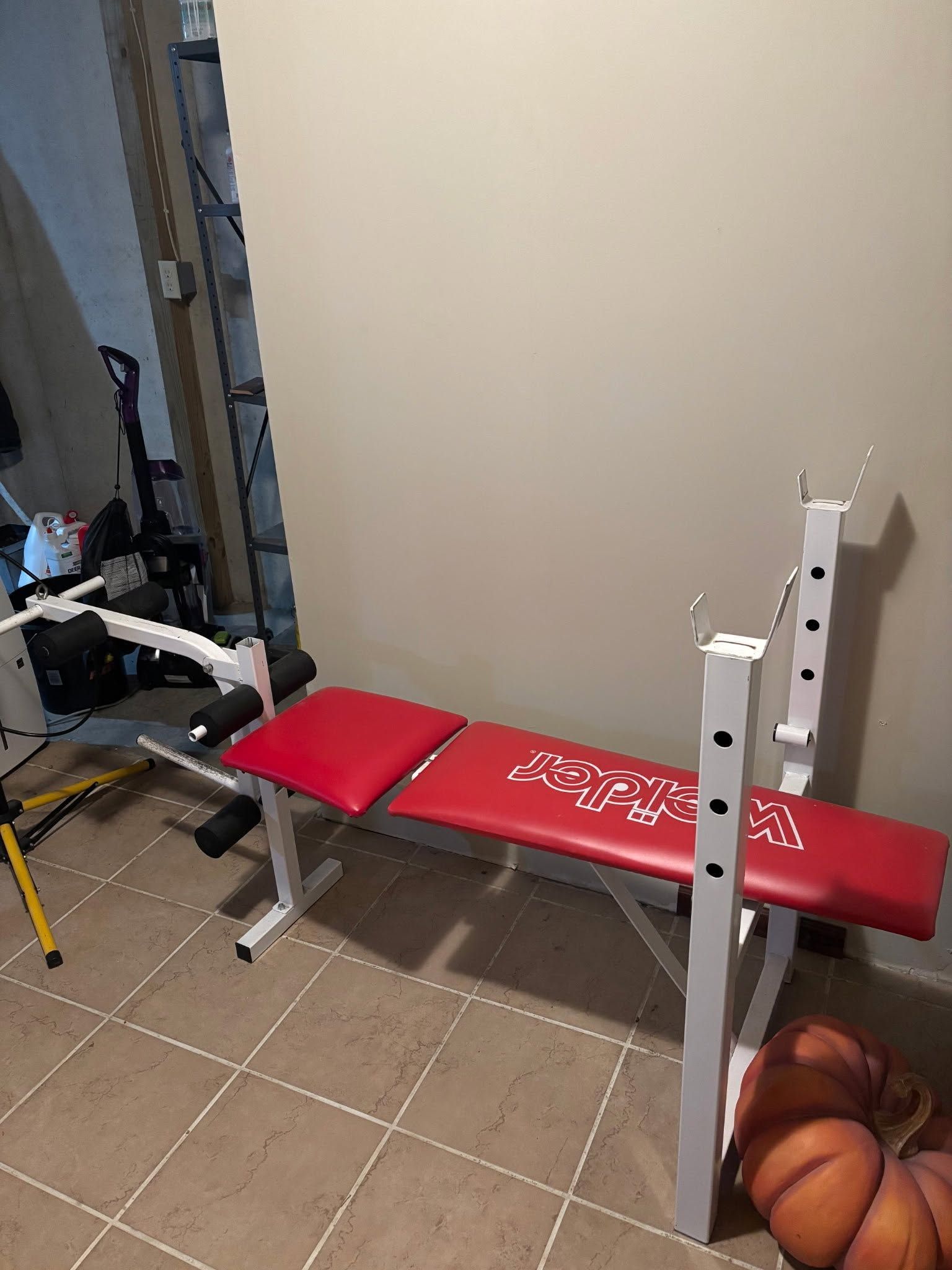 Red weight bench and rack in a tiled room, with basketballs on the floor beside it.