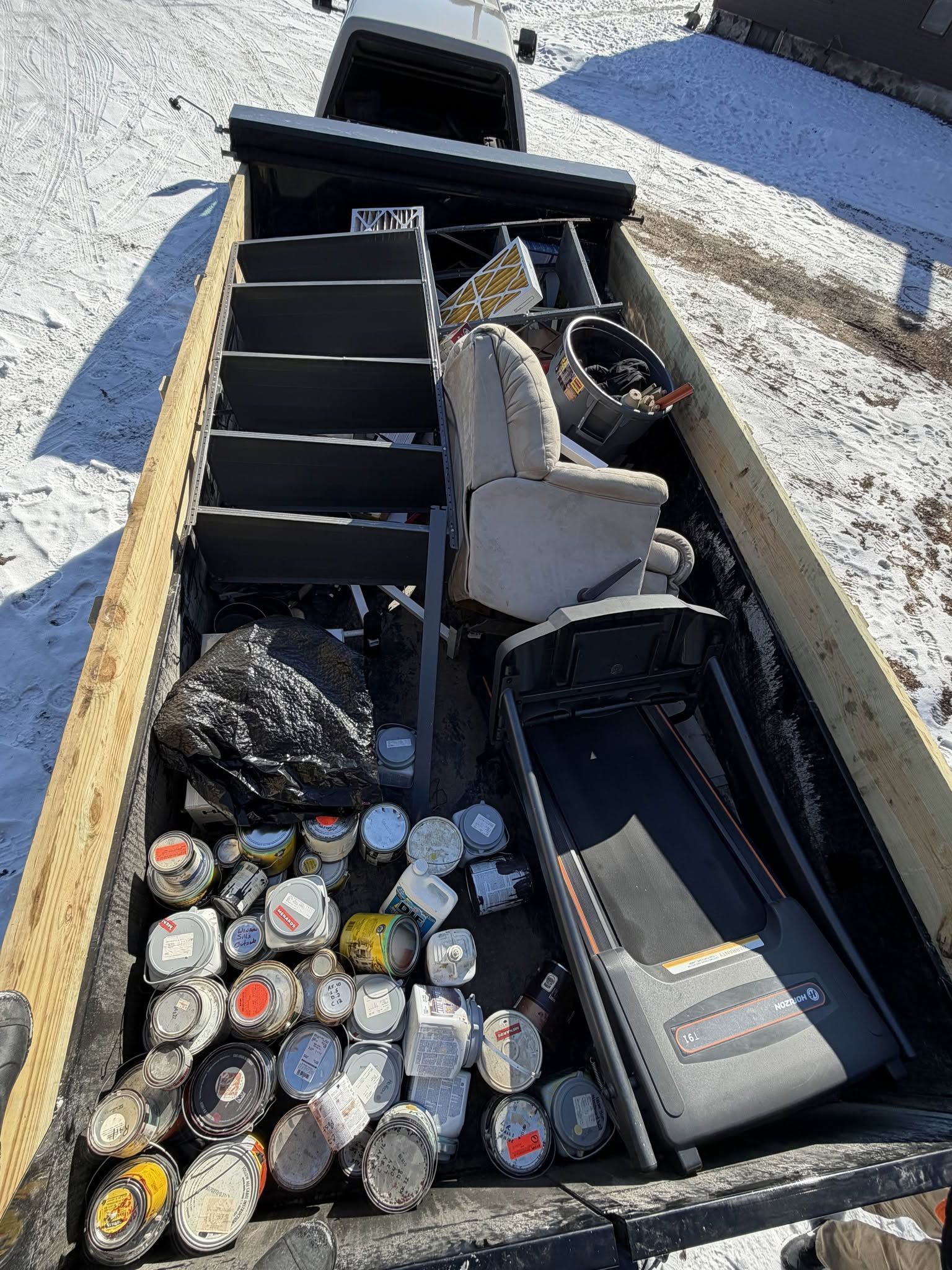 Open trunk packed with assorted tools, supplies, and bottles on a gravel surface.