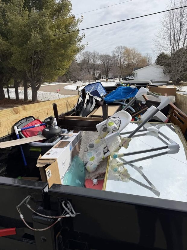 Curbside trailer piled with furniture, bags, and debris on a snowy residential street