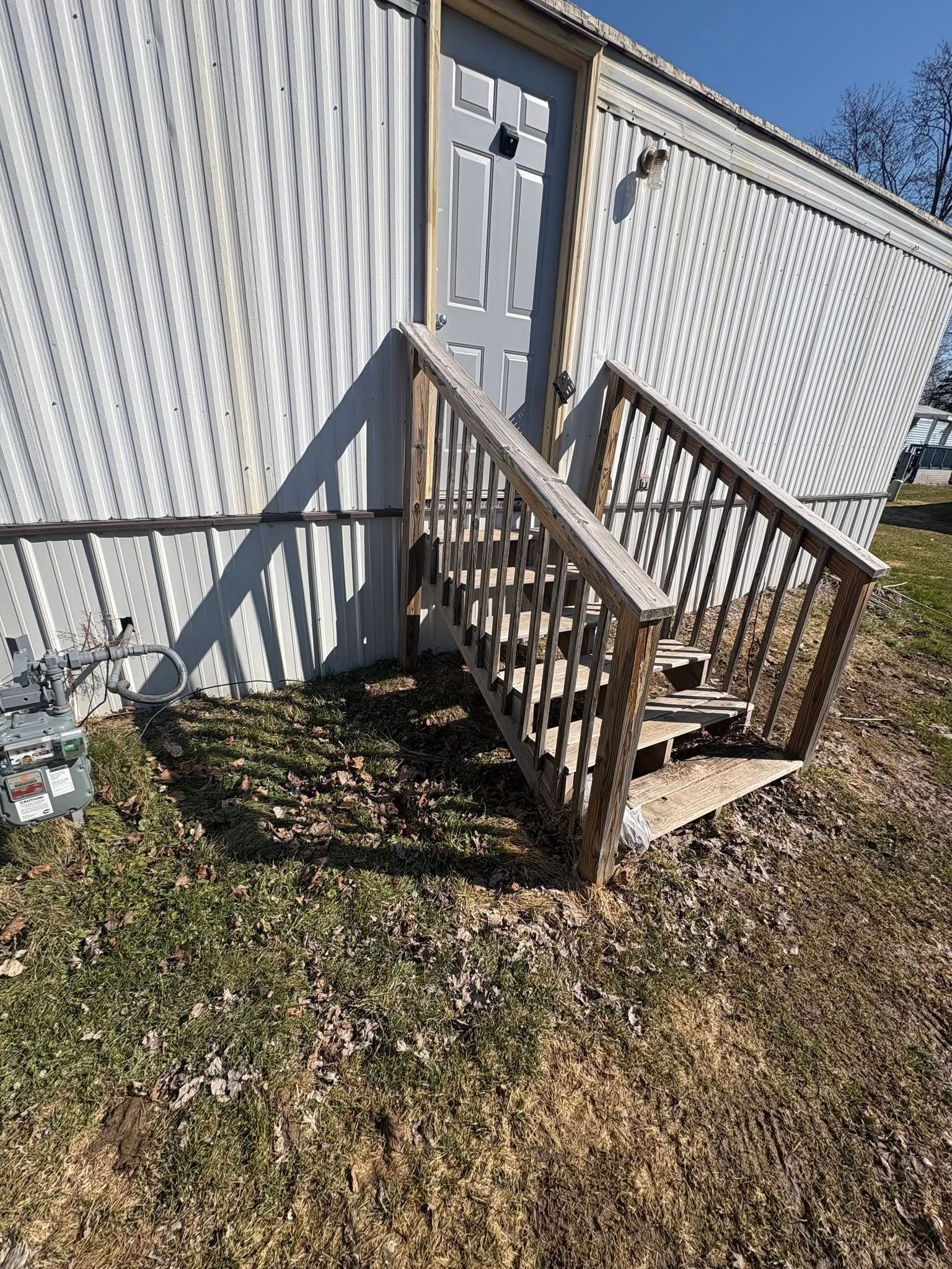 Wooden steps leading to a side door on a white corrugated building, with a small landing and railing.