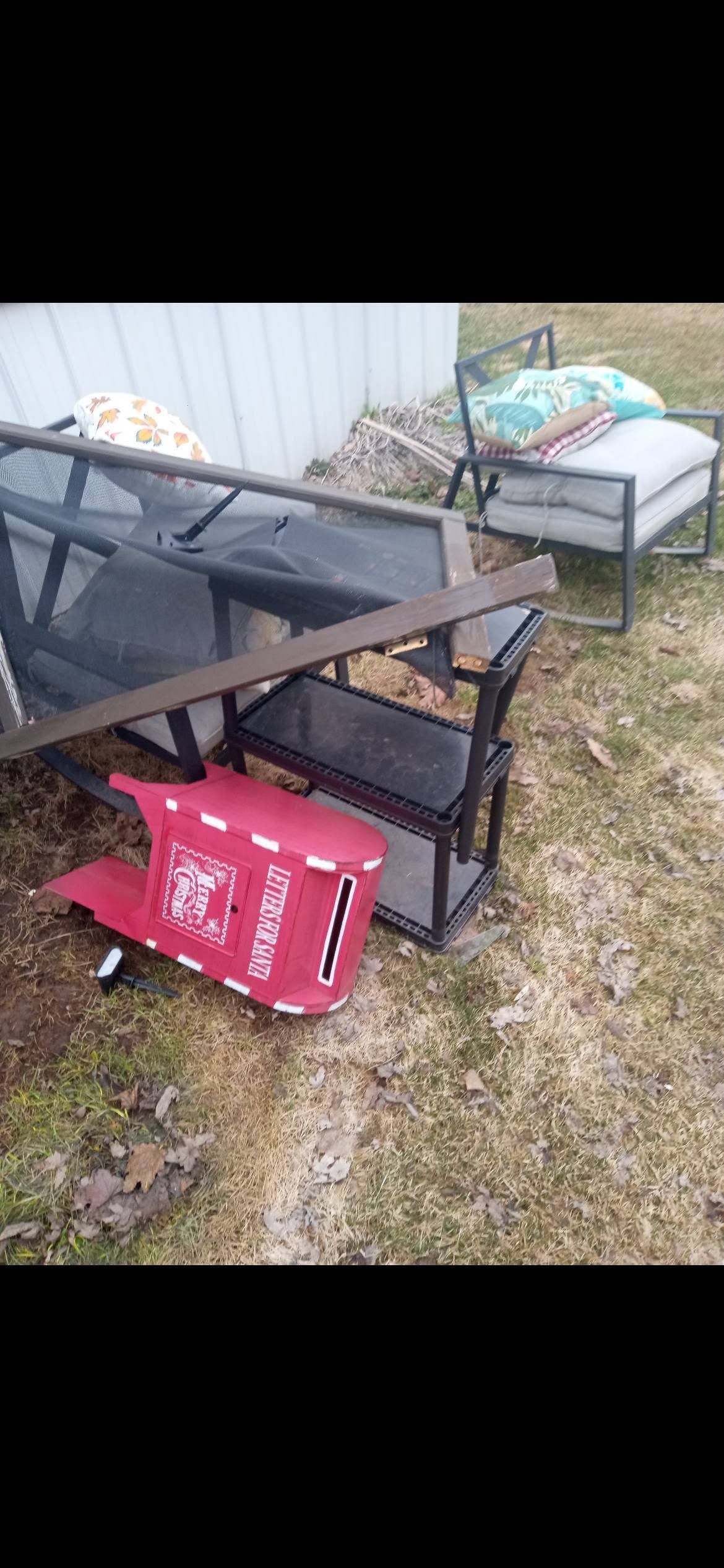 Broken outdoor shelf and red cabinet toppled in a yard beside a white wall