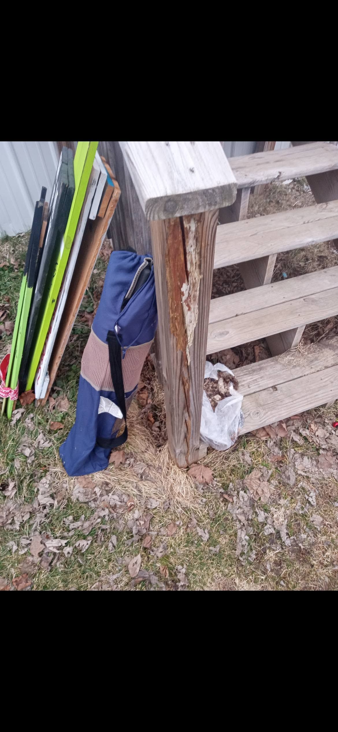 Pallet leaning on fence beside folded blue tarp and long colorful boards on gravel
