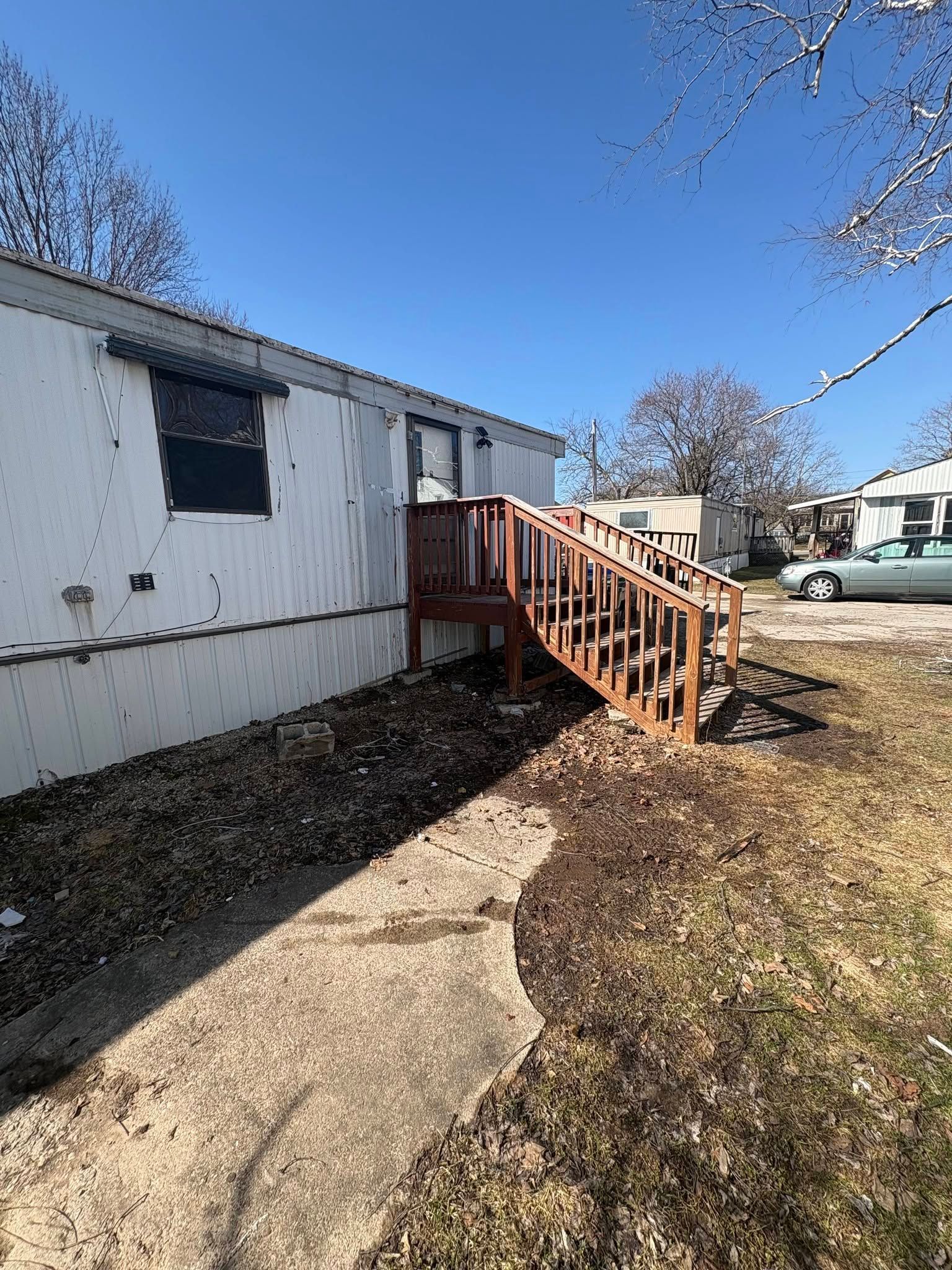 Mobile home exterior with wooden steps and ramp, bare trees, and a clear blue sky