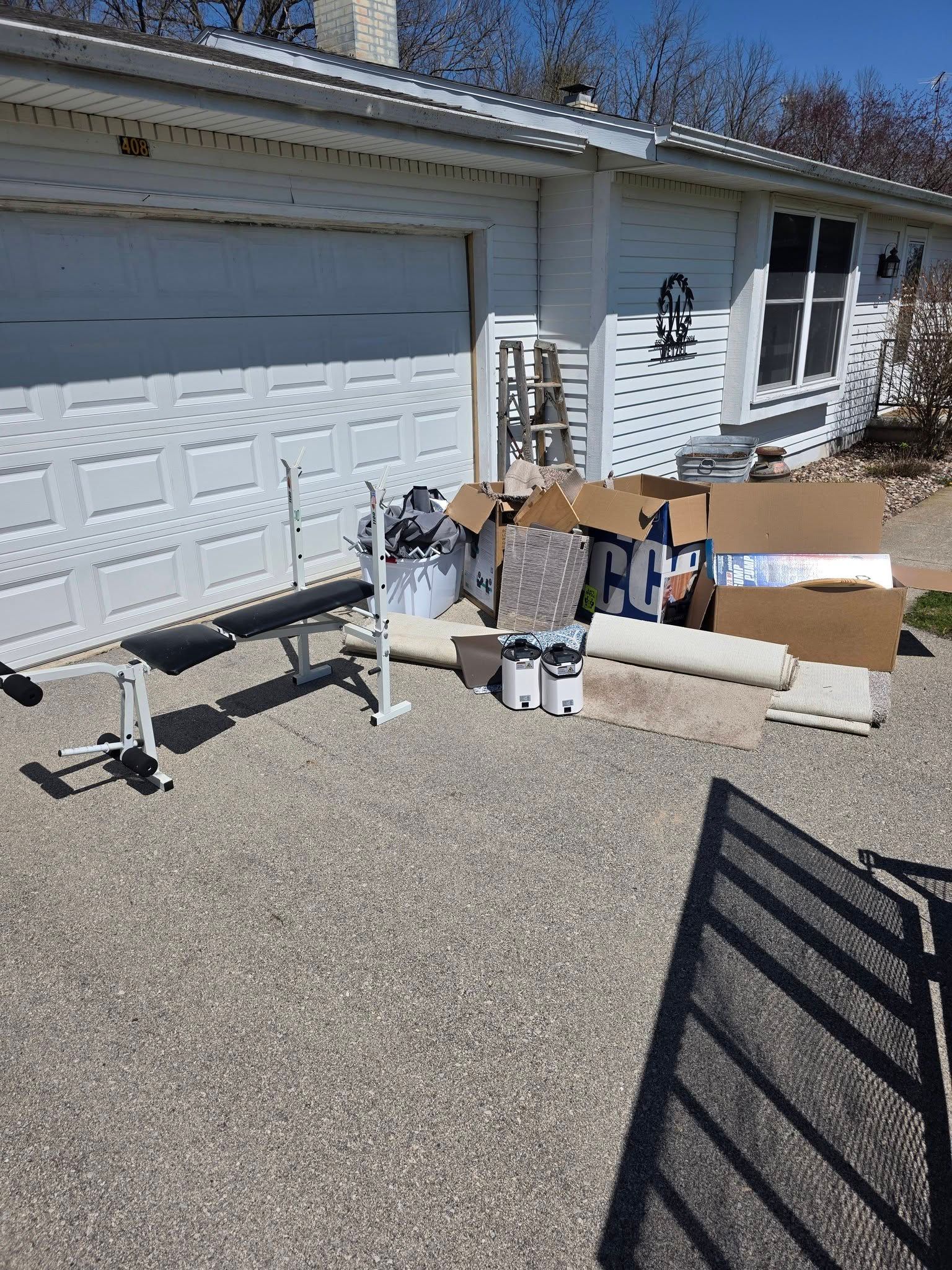 Boxes and furniture outside a garage beside a white house on a sunny day