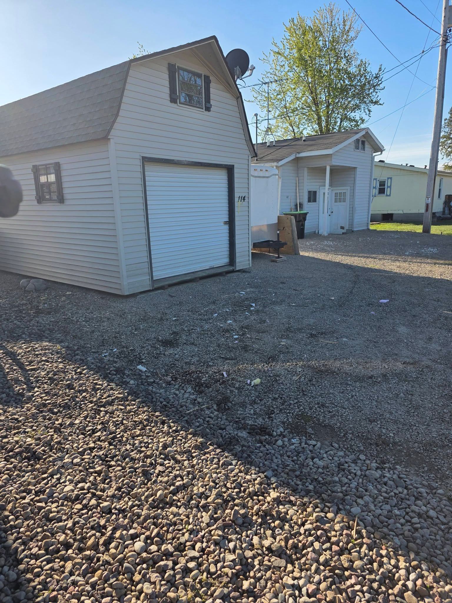 White garage with closed door beside a white house on a gravel driveway in sunlight