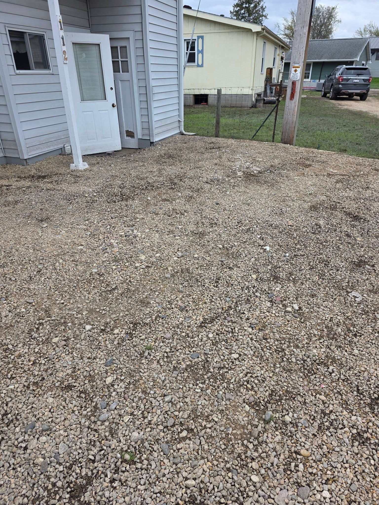 Gravel-covered yard beside a white shed and house, with a fence and parked truck in the background.