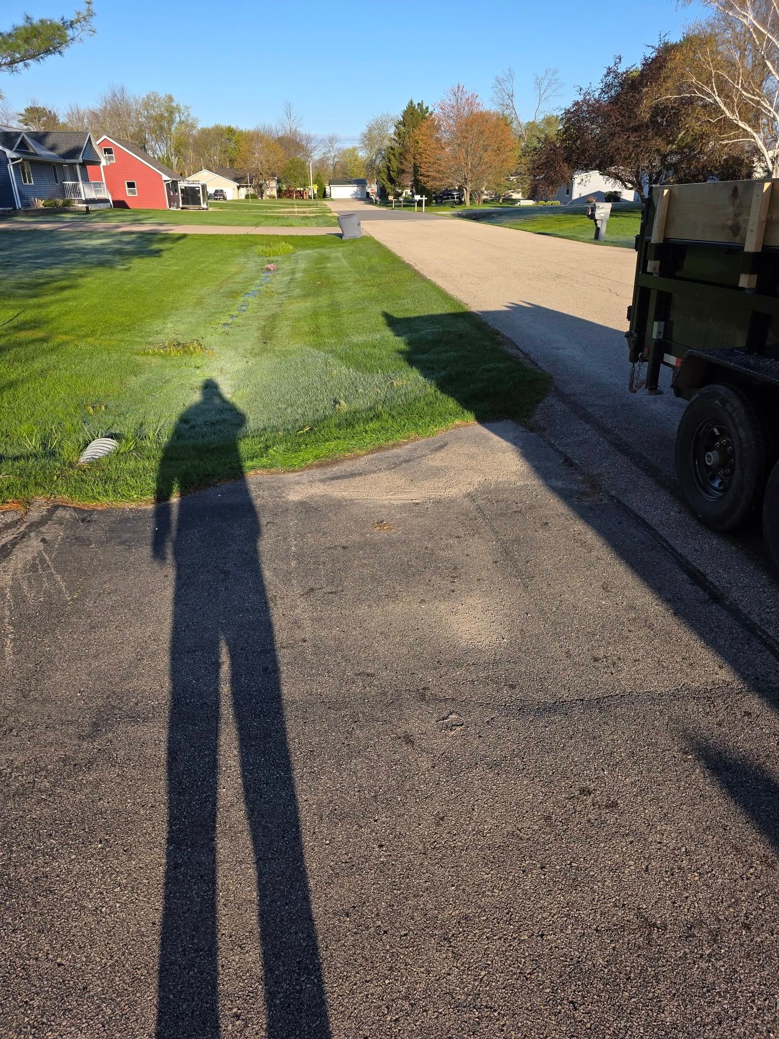 Long shadows on a paved path beside a grassy lawn and houses on a sunny day