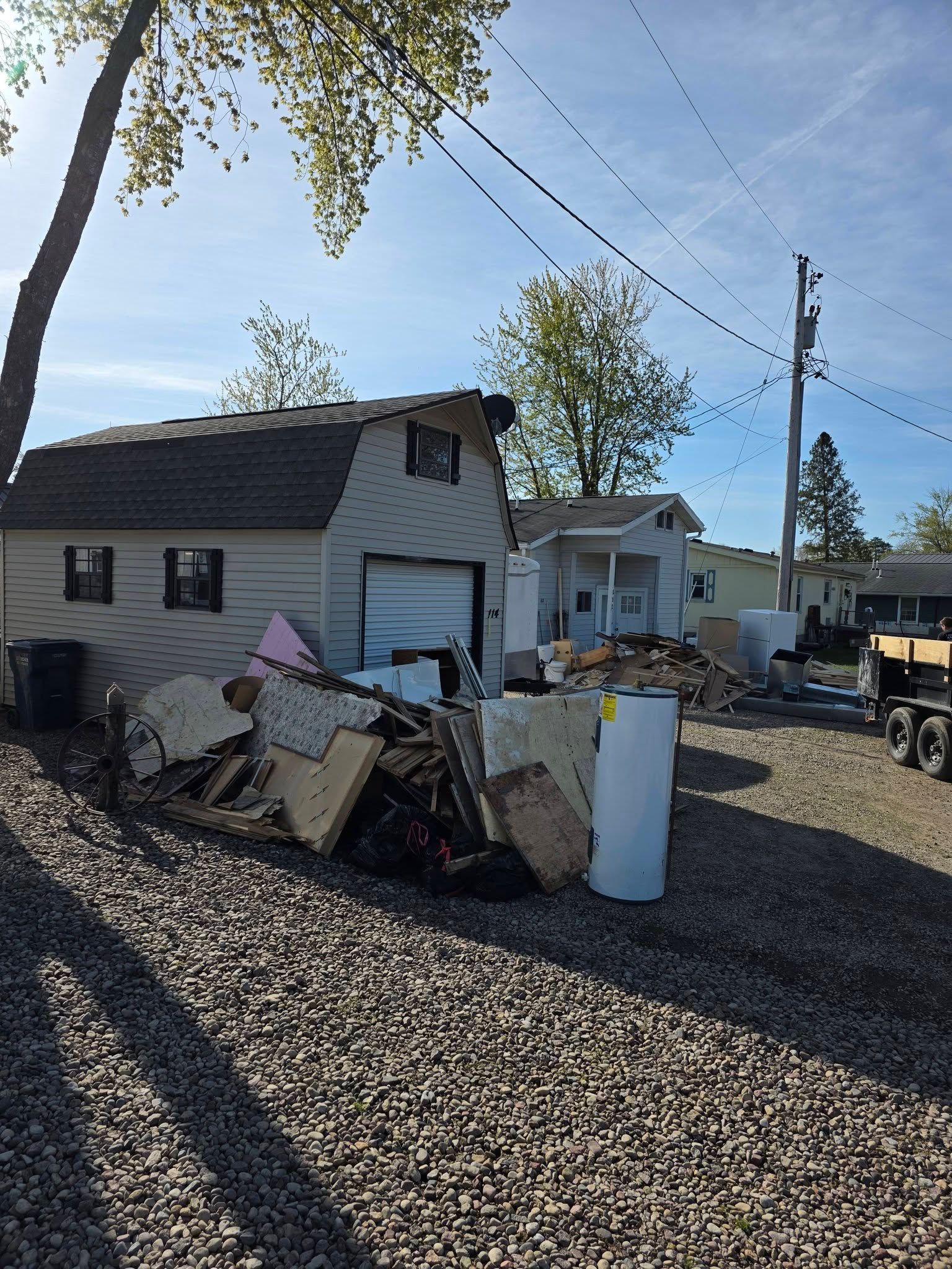Small house with a cluttered pile of debris in the yard, under a clear blue sky.