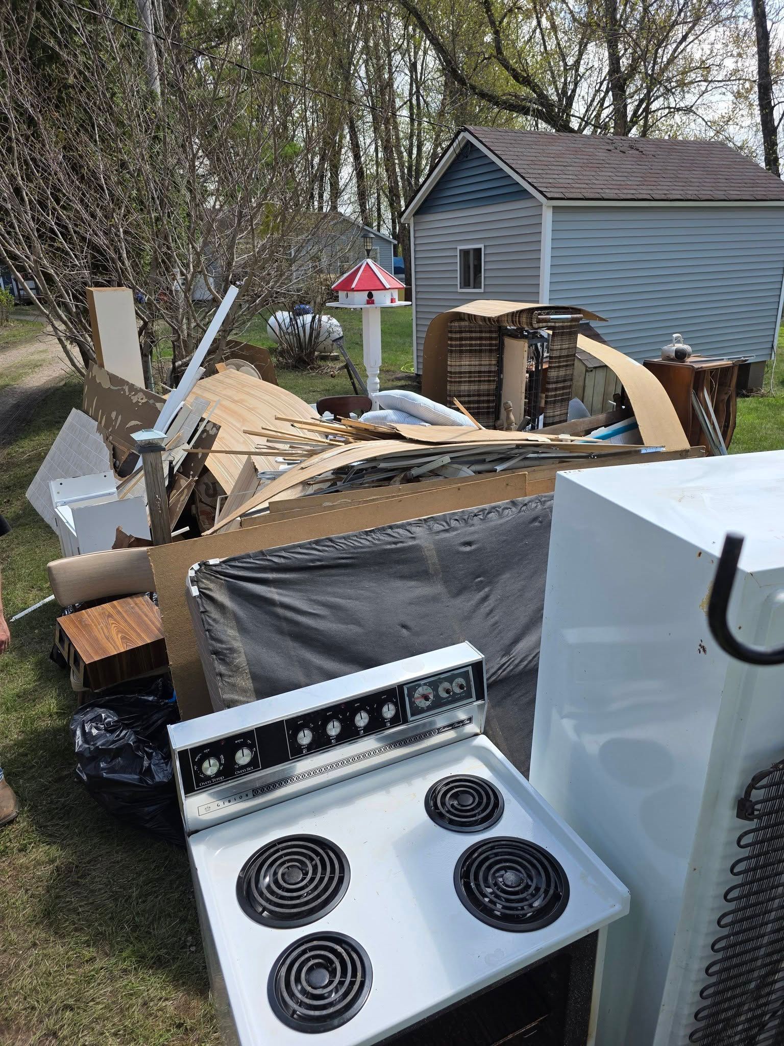 Outdoor cluttered yard with a white electric stove in front of debris and a shed.