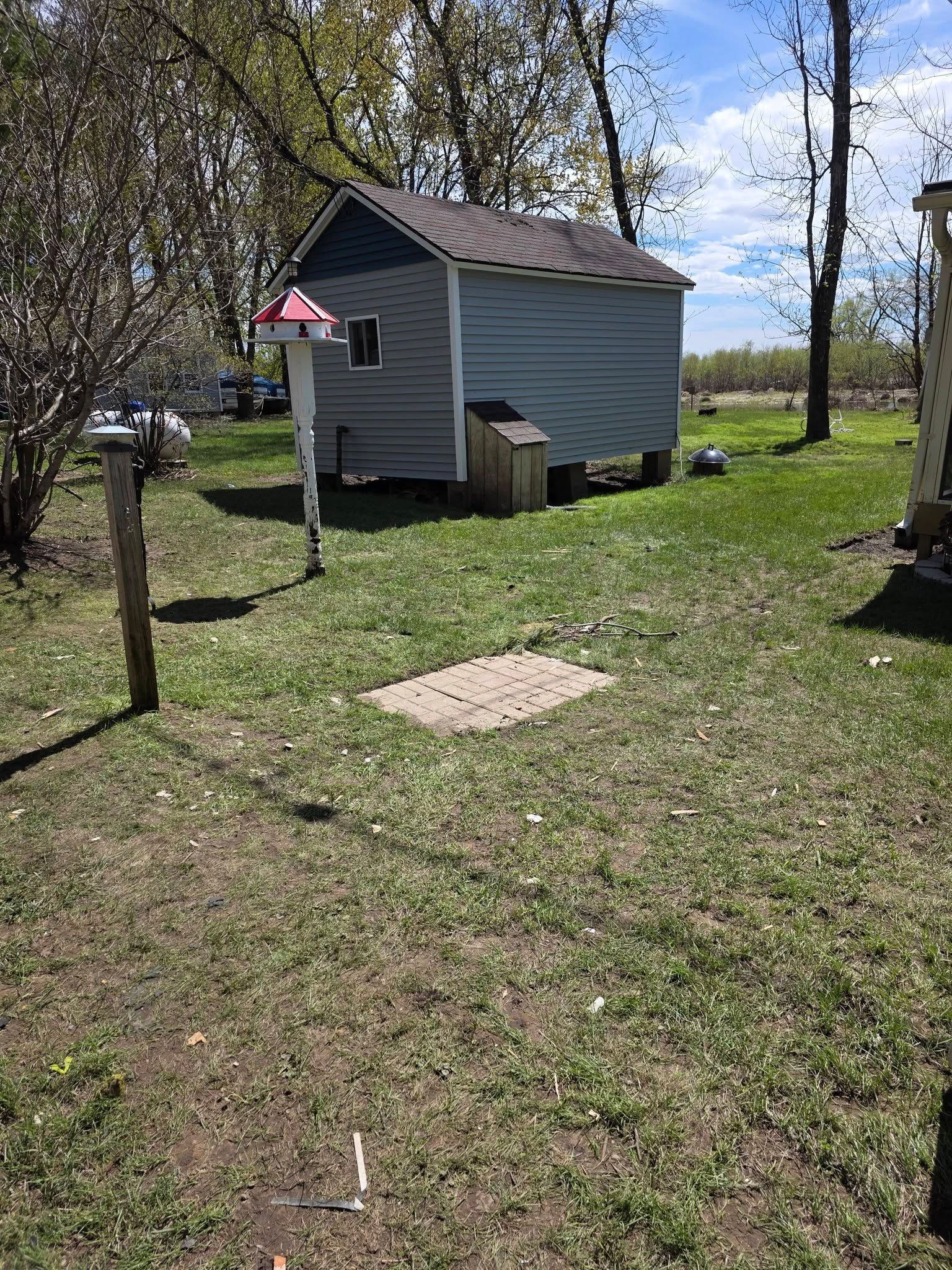 Small blue shed with a red birdhouse in a grassy yard under partly cloudy skies.