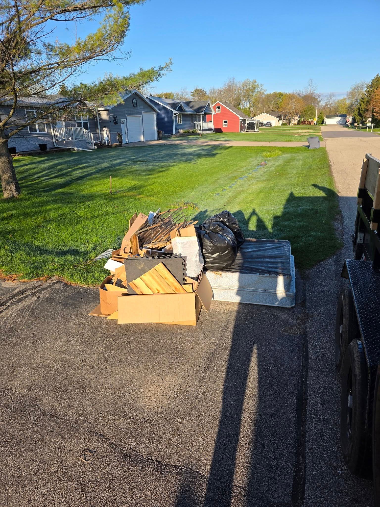 Cardboard boxes and trash bags by a curb beside a grassy yard in a suburban neighborhood