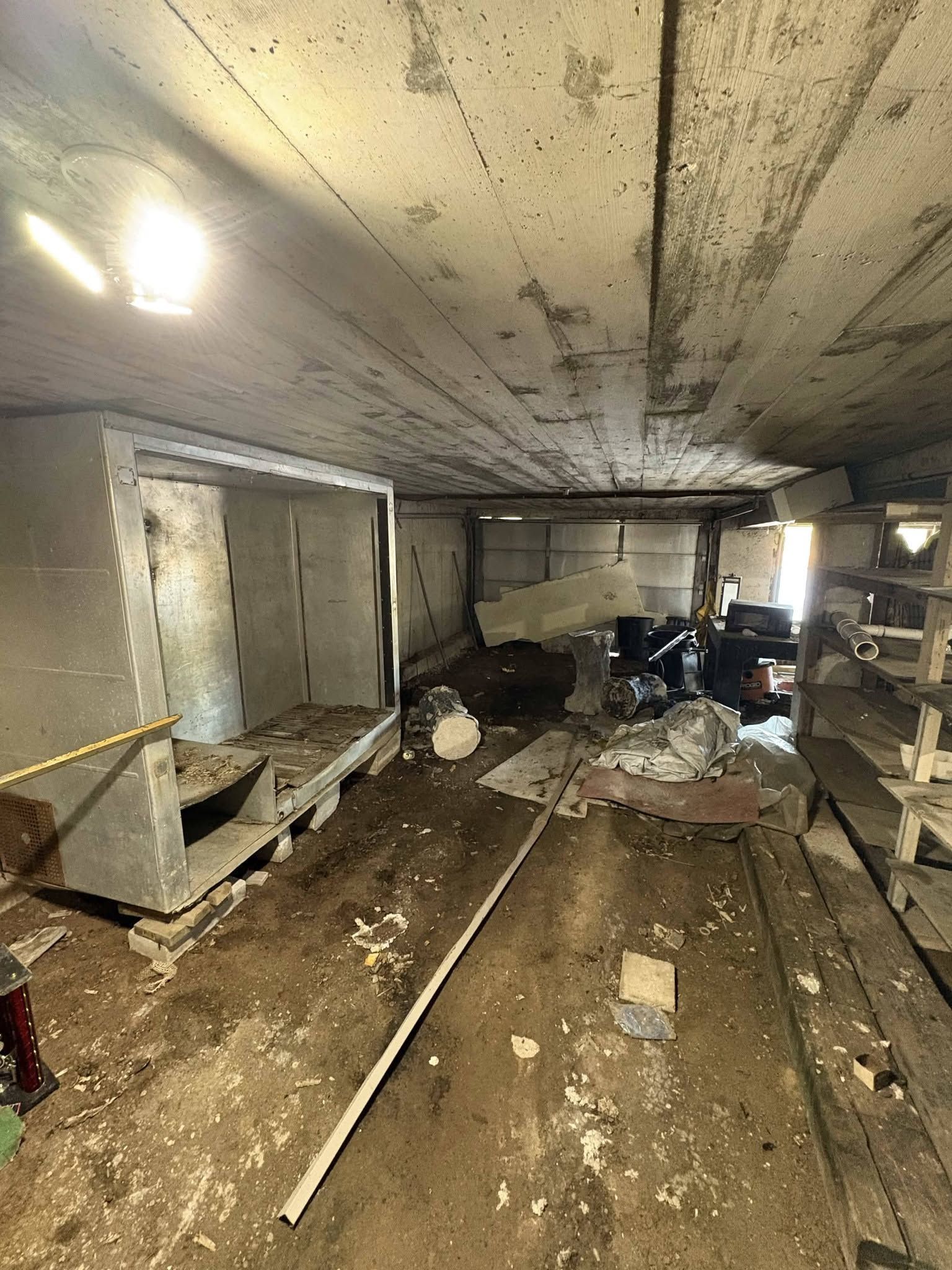 Damaged basement room with debris, broken ceiling, and exposed framing after flooding or collapse.