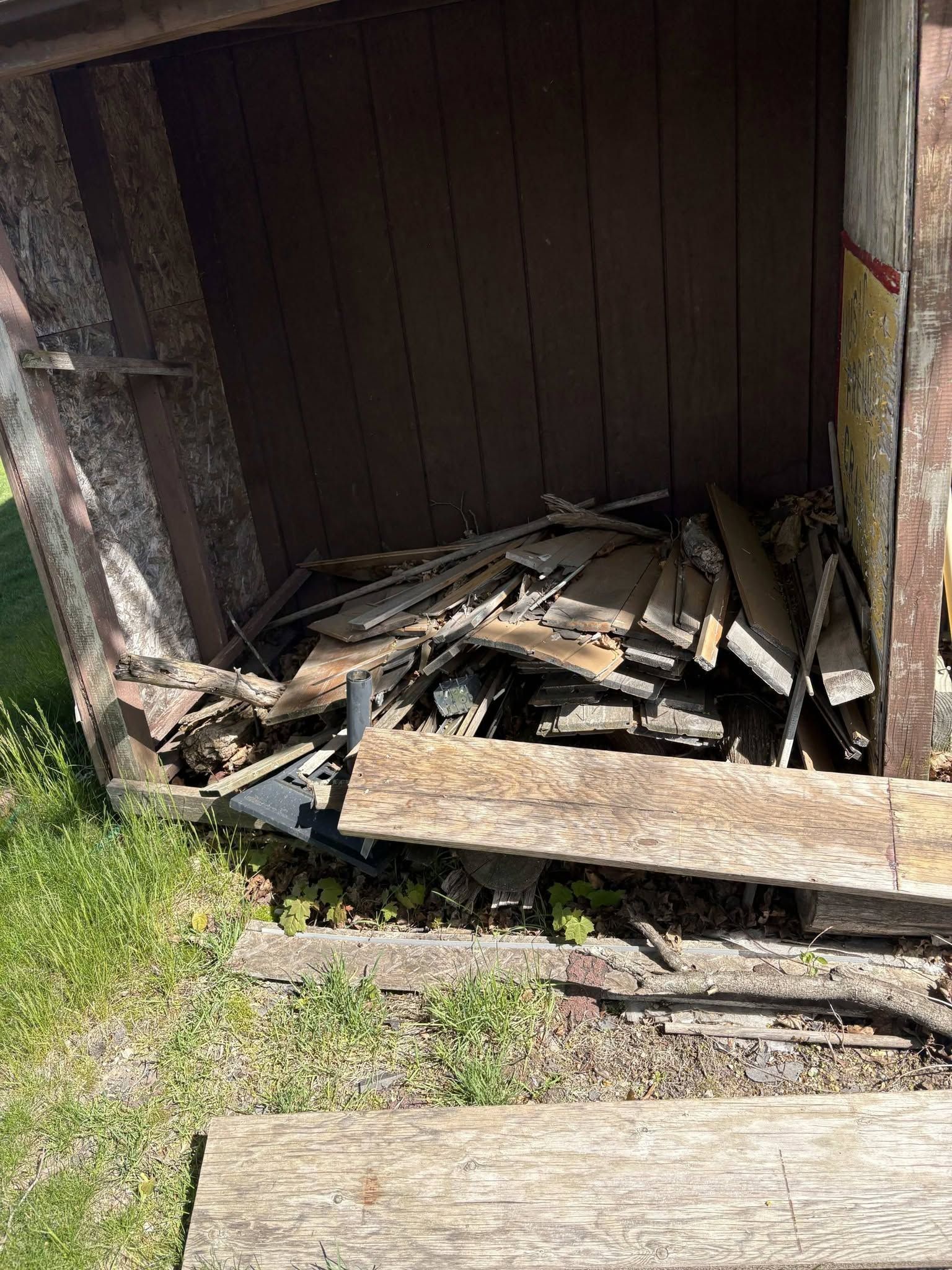 Collapsed wooden shed with a pile of debris and broken boards at the entrance.