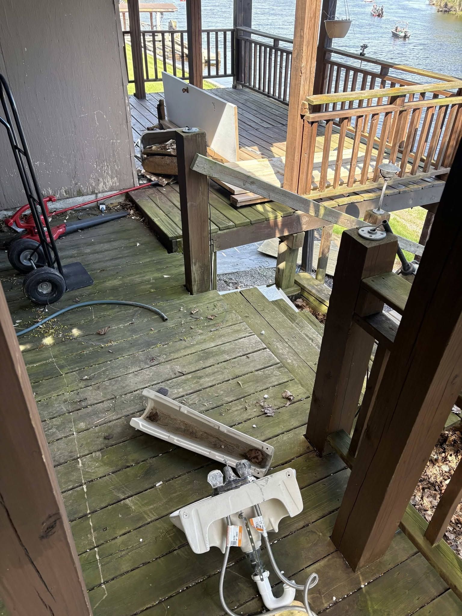 Damaged wooden deck with broken railing and debris, viewed from a patio.