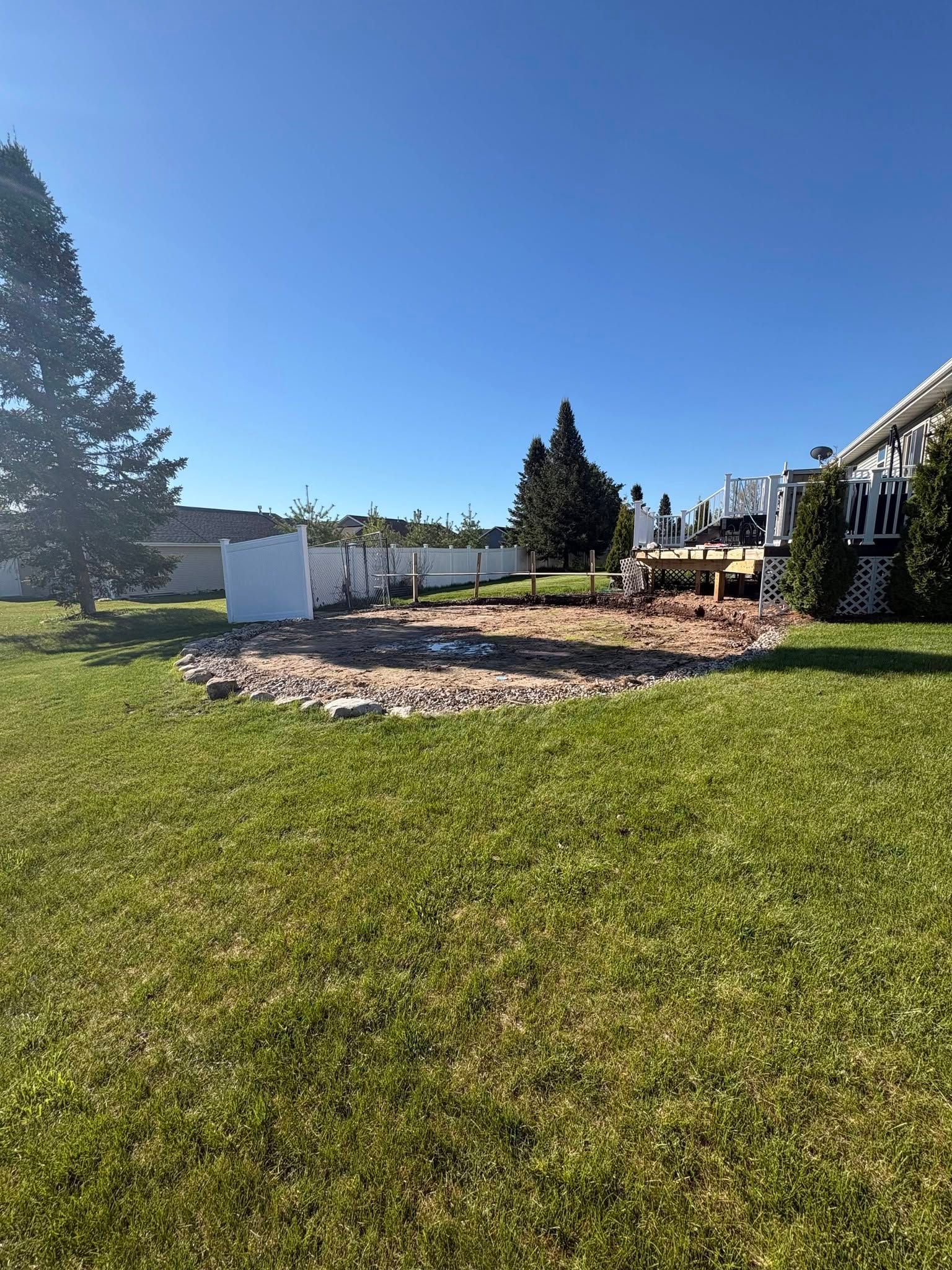 Sunny backyard with green lawn, stone patio, white shed, and wooden picnic table under a clear blue sky