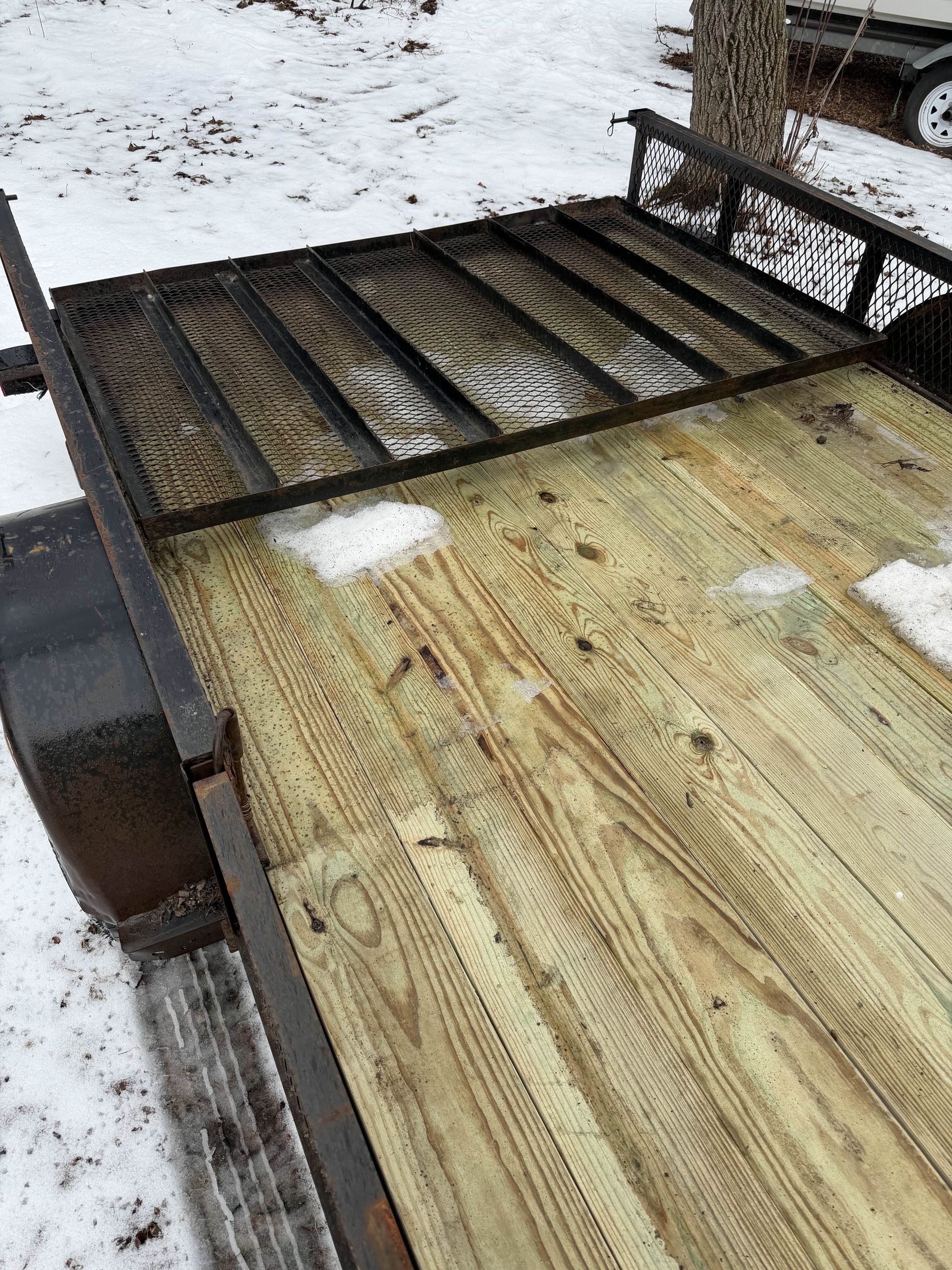 Snow-dusted wooden trailer bed with a black metal frame and side rail outdoors