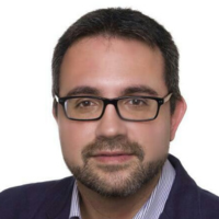 Hombre con gafas y barba, vestido con chaqueta, mirando a la cámara.