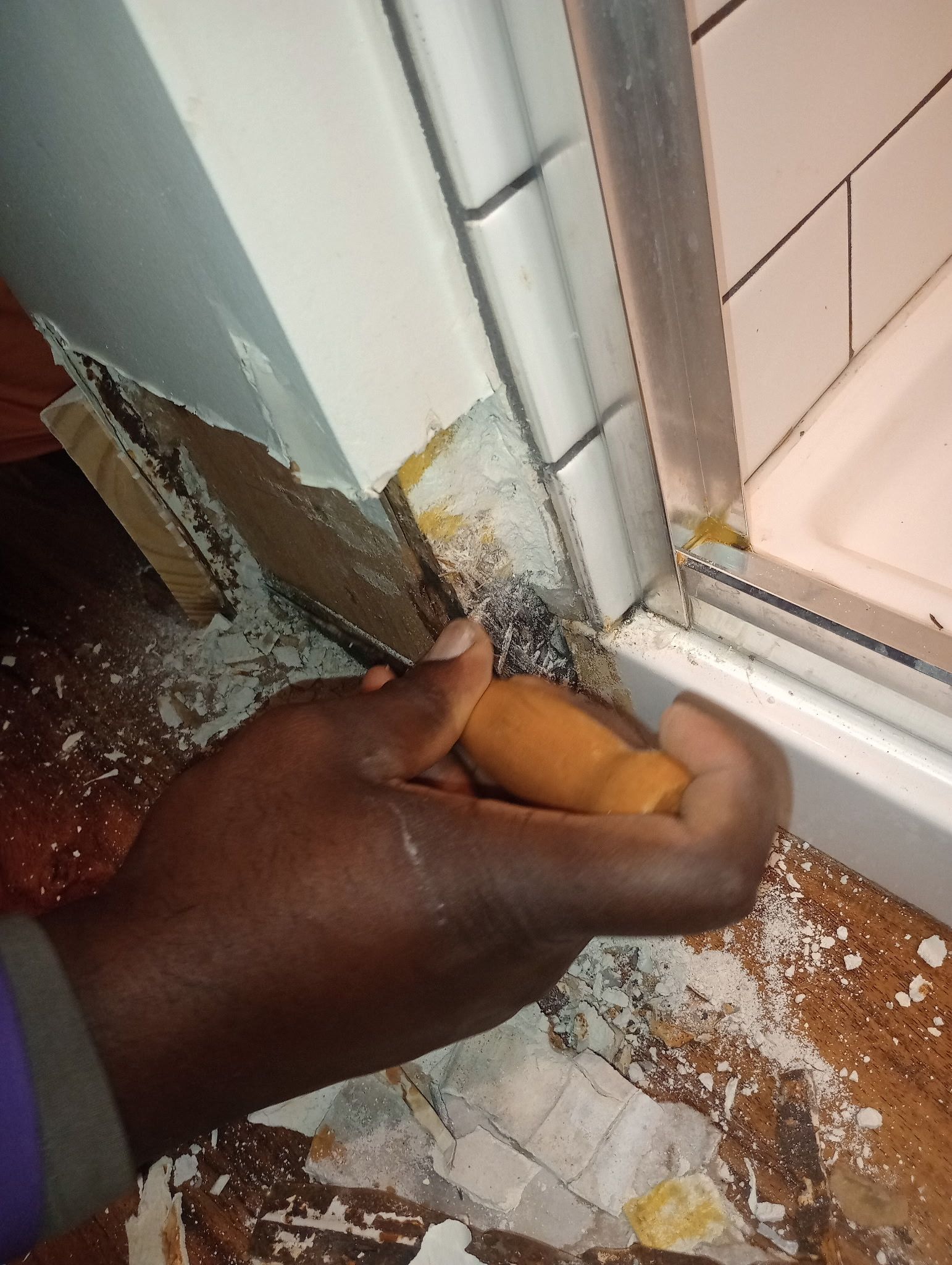 Hand repairing a damaged door frame with debris on the floor near a tiled wall