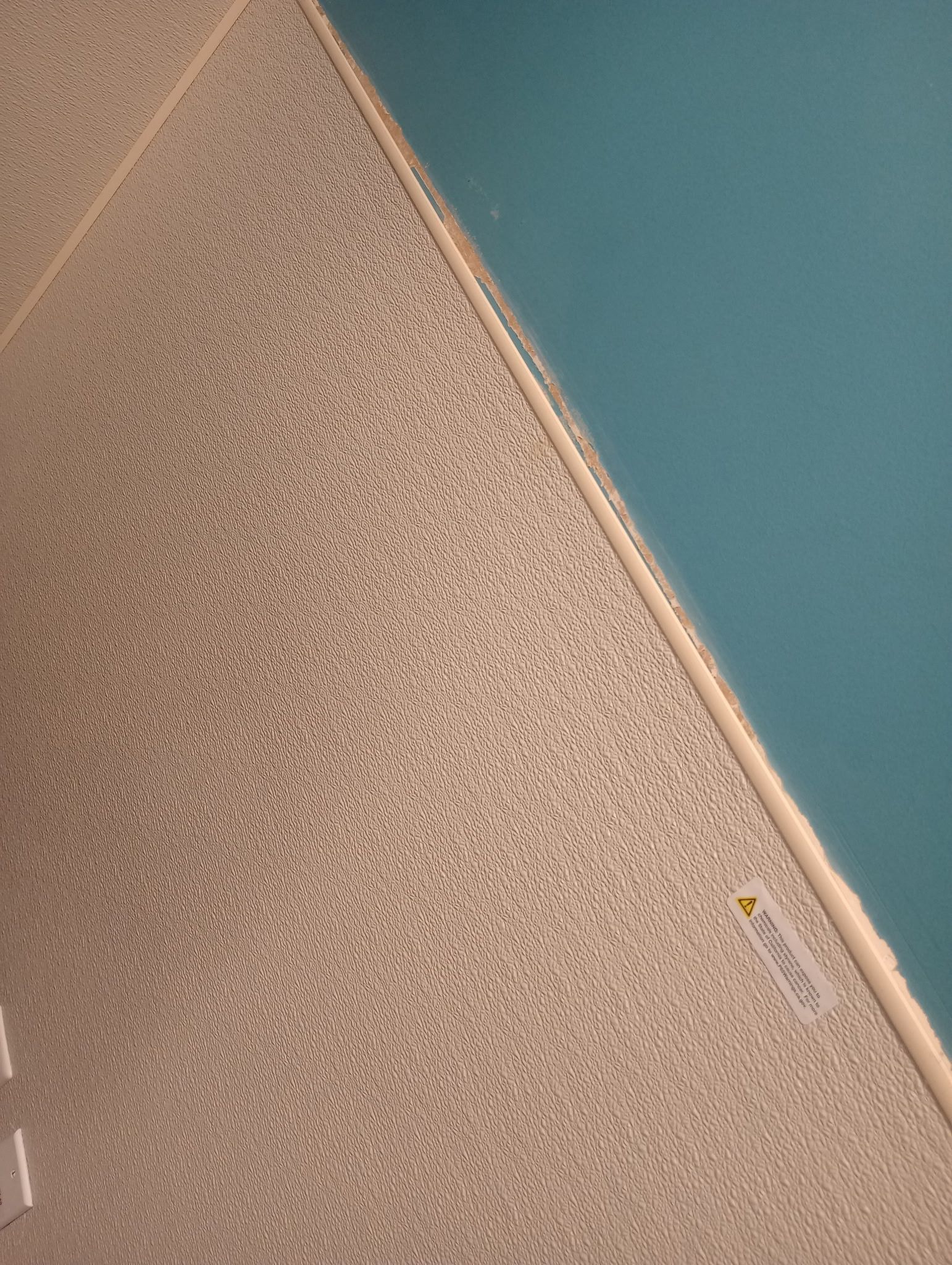 Close-up of a textured beige ceiling meeting a teal wall at a diagonal seam.