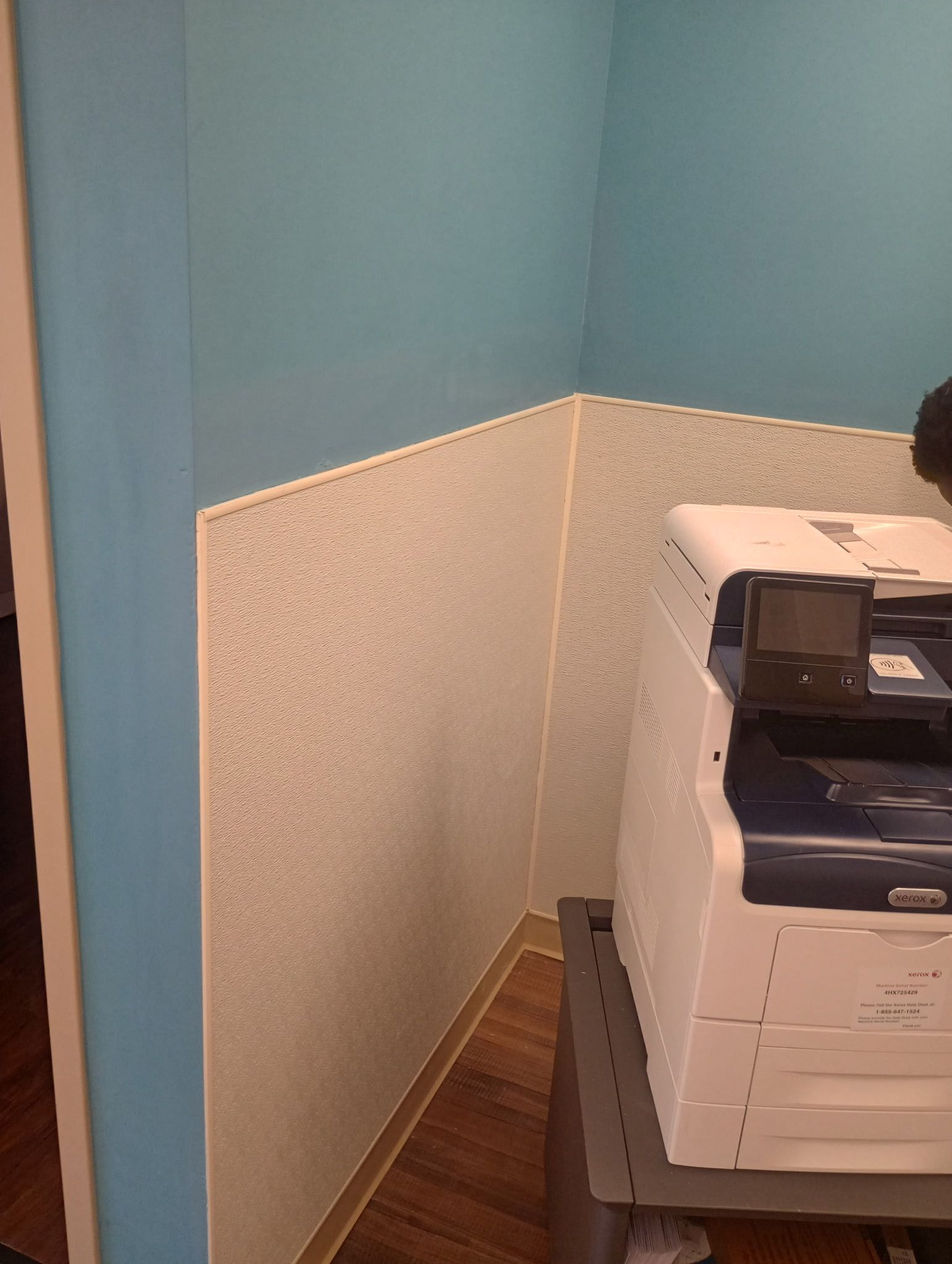 Narrow hallway corner with blue and beige walls, wood floor, and a printer/copier on the right.