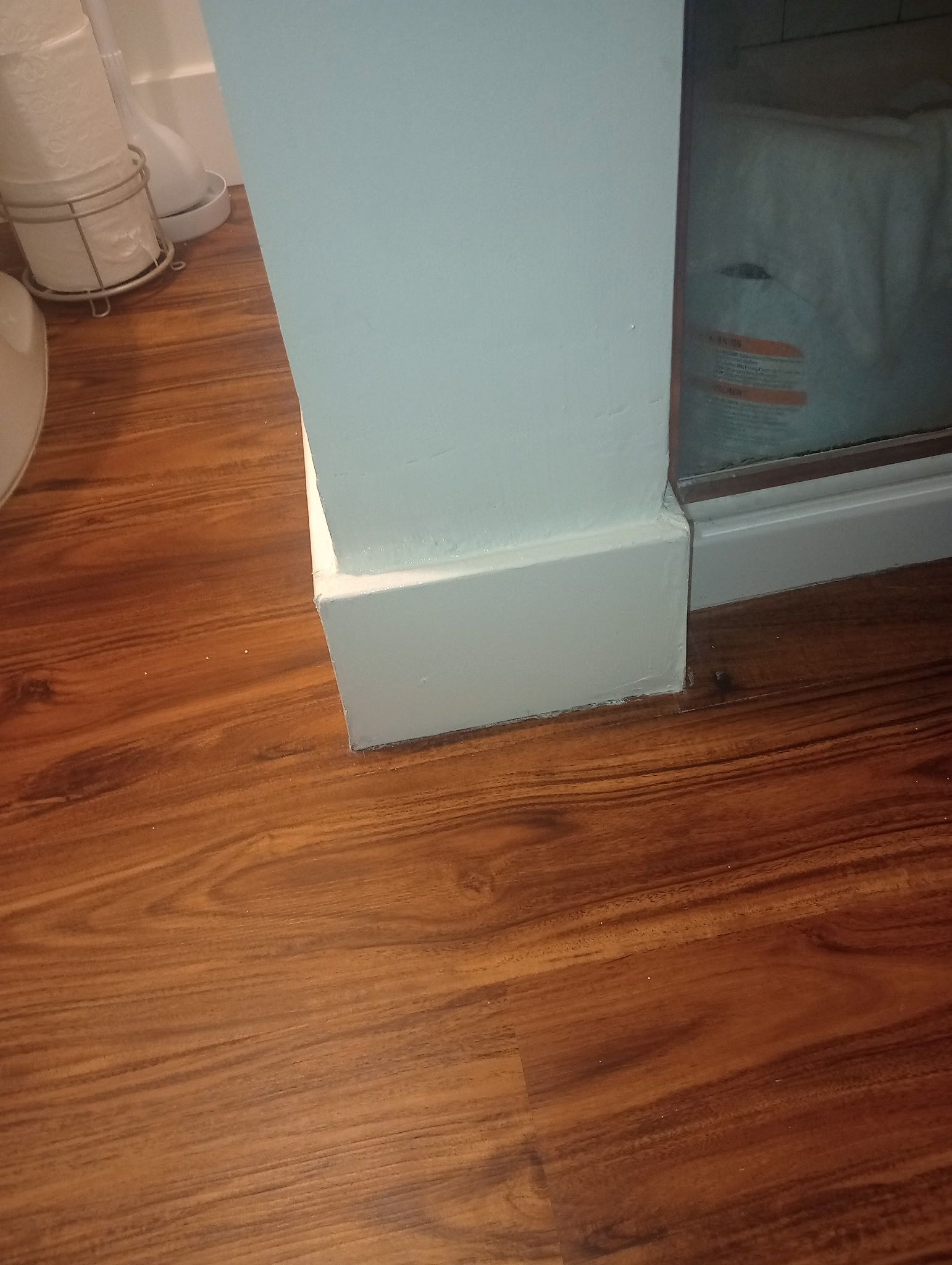 Corner of a room with a light blue wall, white baseboard, and wood floor beside a gray cabinet.