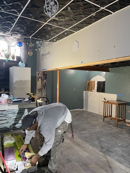 Man working on construction project in a room with gray walls, ceiling tiles, and a gray floor.