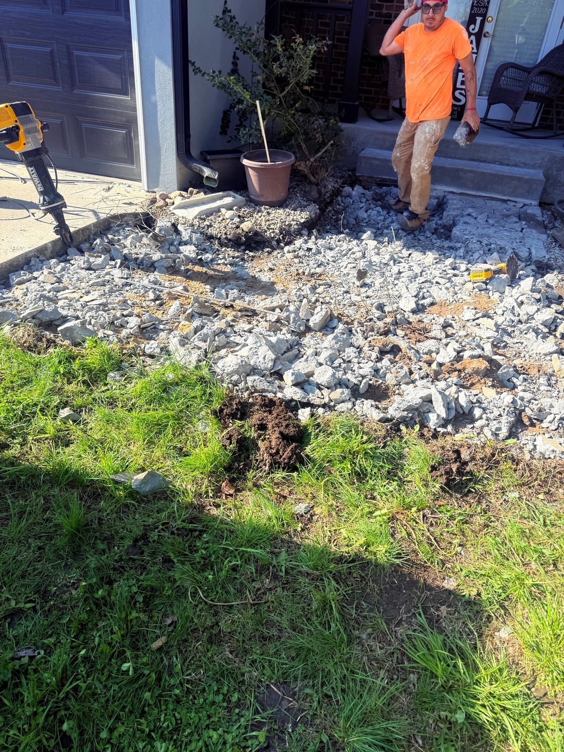 Person in orange shirt standing by a front porch with rubble and damaged ground in the yard