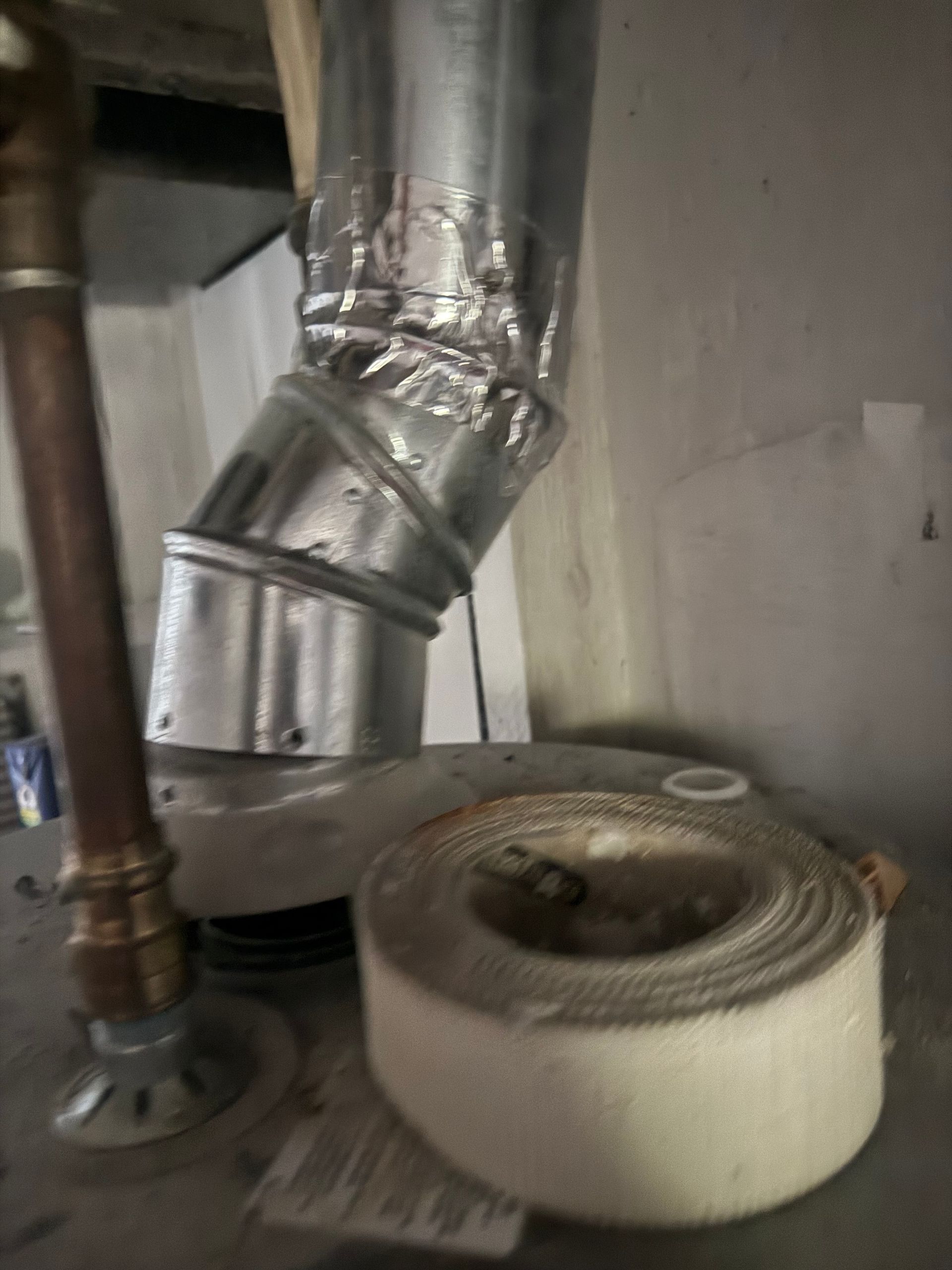 Insulated metal ducting and a white coiled hose inside a basement or utility room.