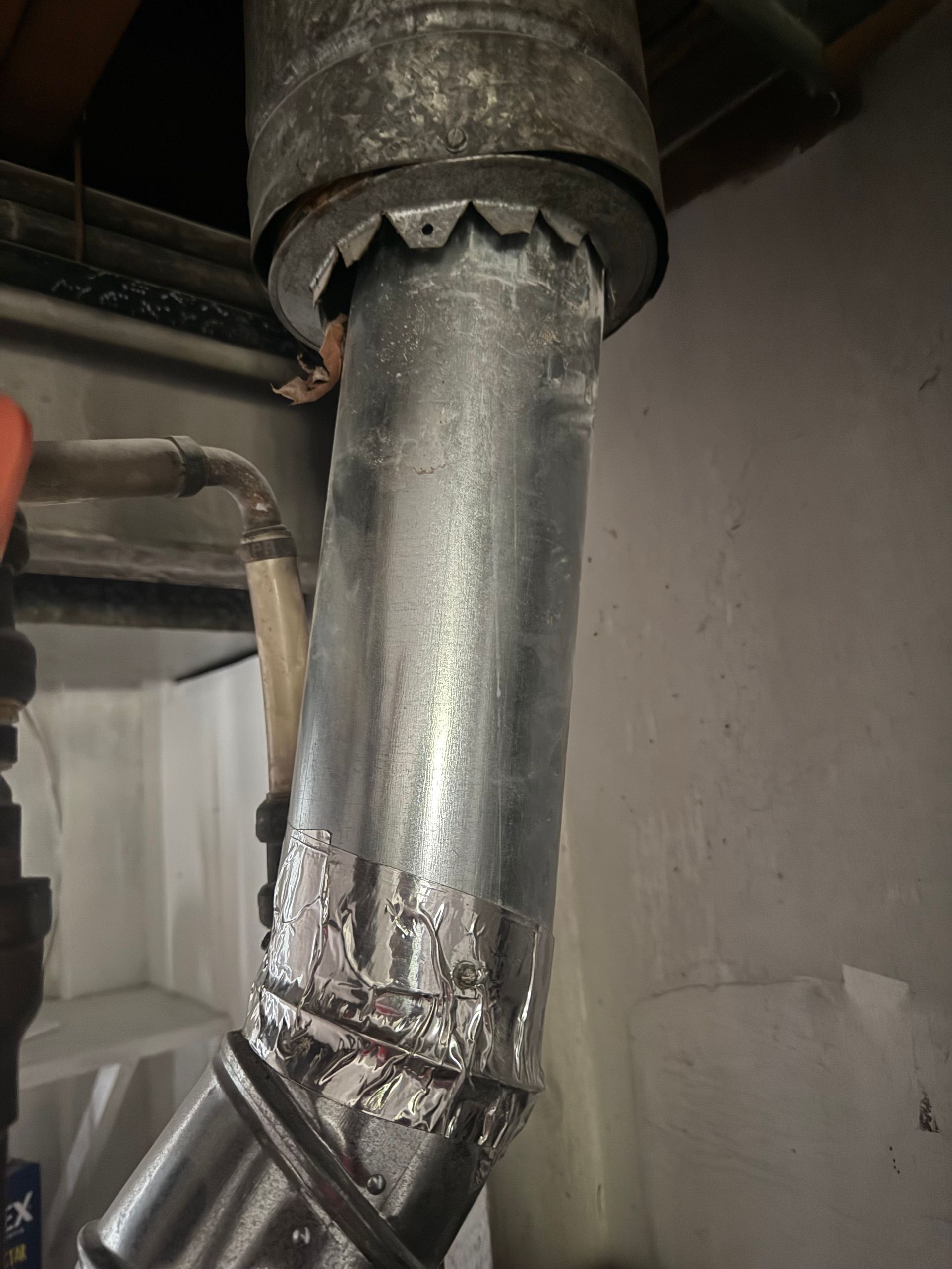 Metal duct pipe with a taped joint and jagged opening inside an industrial space