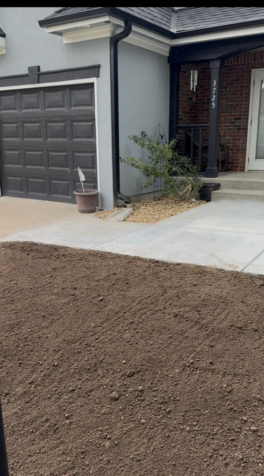 New concrete driveway beside a dark garage, with a small plant near the front entry.