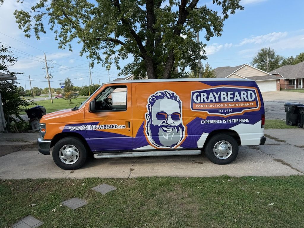 Orange and purple Graybeard van parked in a driveway beneath a tree