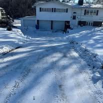 Snow-covered driveway leading to a house with snow on the roof.