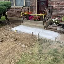 Newly poured concrete walkway with a brick house and decorative flower pots.