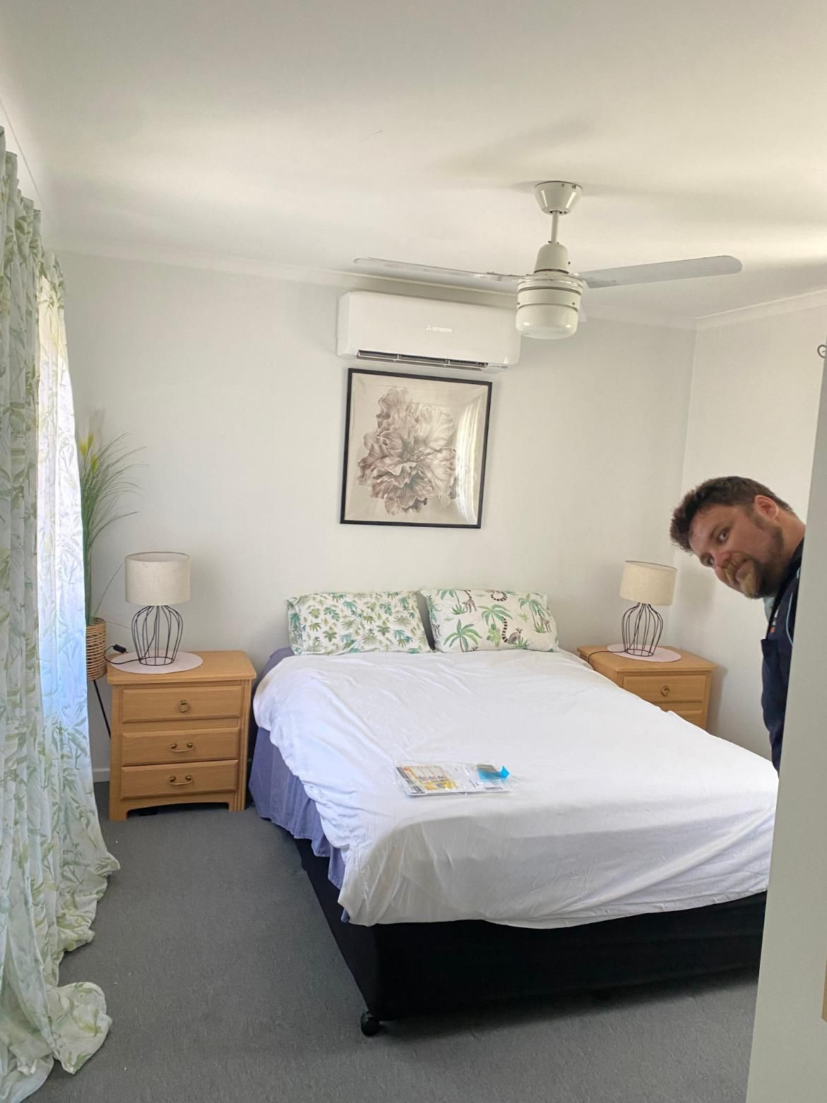 Man is Standing in a Bedroom With a Bed and a Ceiling Fan — Brenden Wilson Electrical in Elimbah, QLD