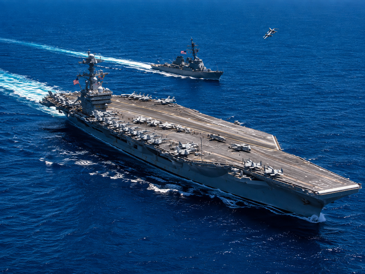 Battleship docked by a waterfront pier on a calm day, with gray-green hull and tall superstructure.