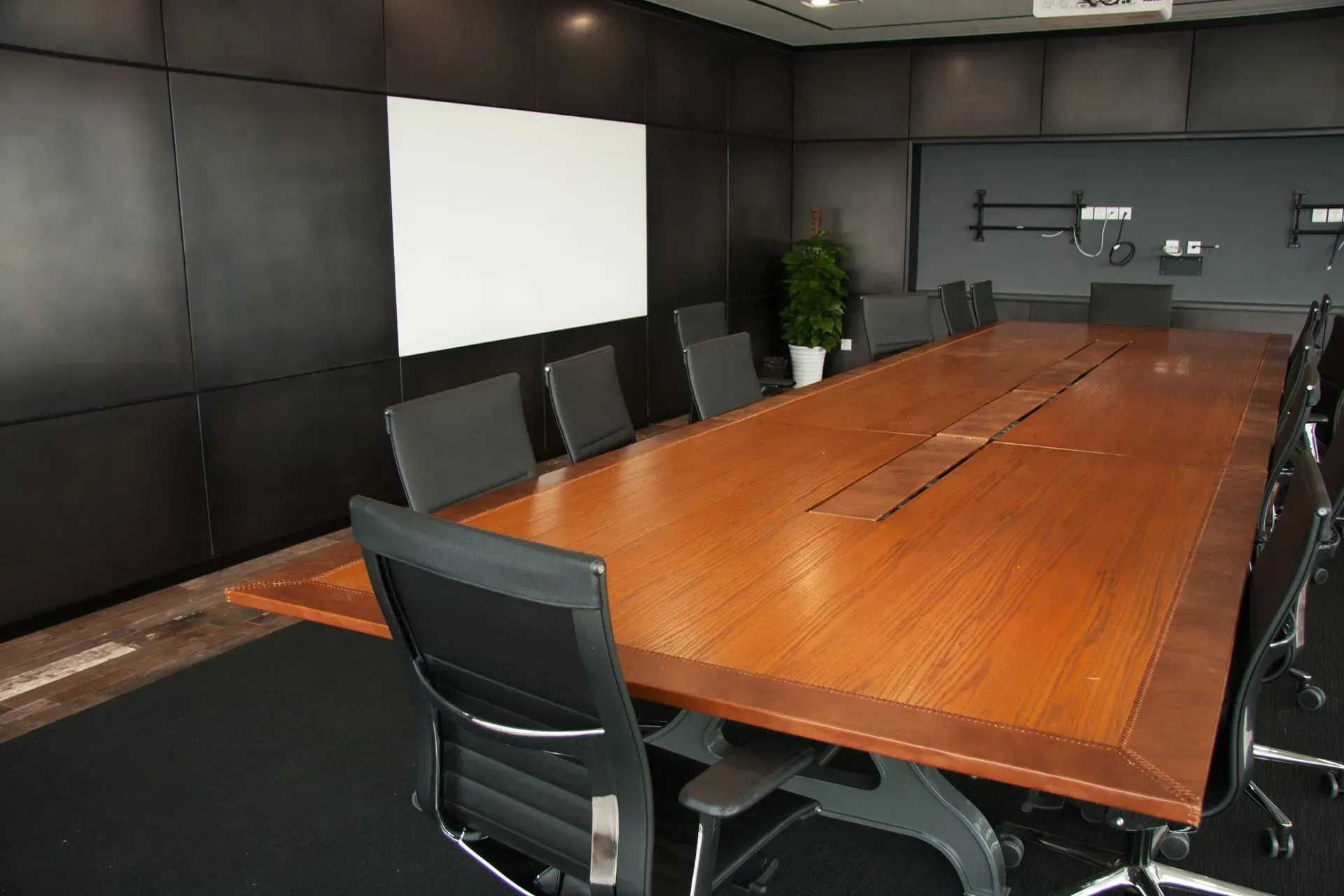 Empty conference room with a long wooden table, black chairs, and dark walls