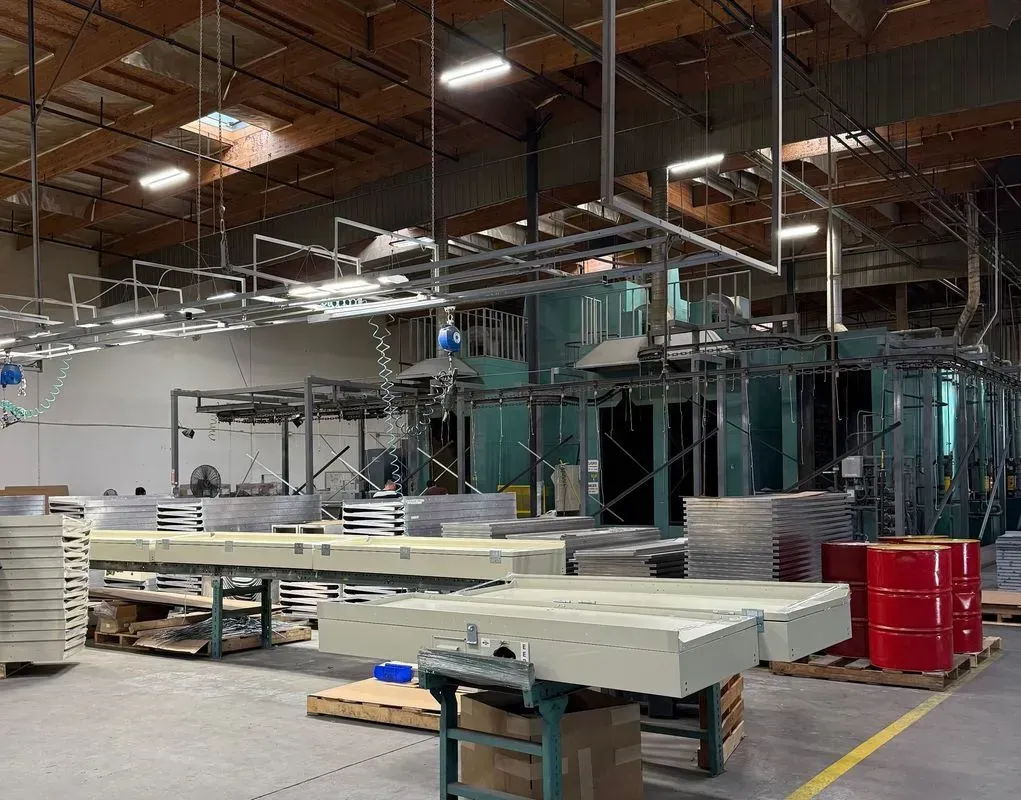 Industrial workshop with large teal machinery, stacked materials, and red bins under an unfinished ceiling.