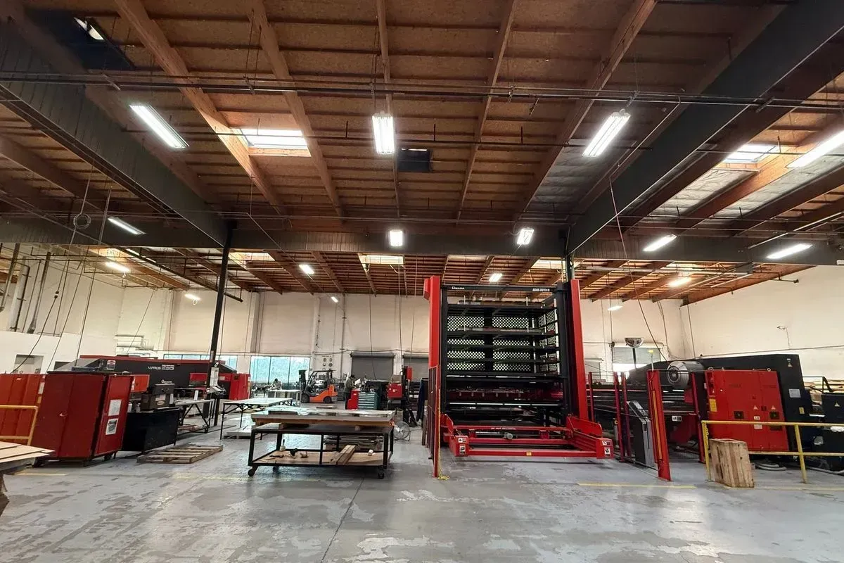 Wide warehouse interior with red industrial machines, worktables, and high ceiling lights