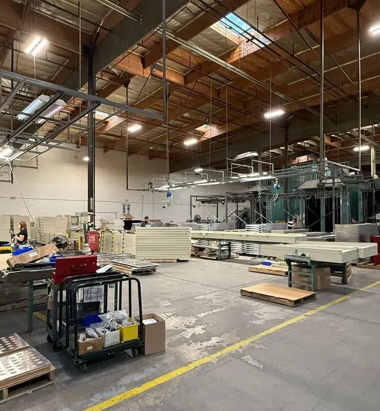 Large industrial workshop with scaffolding, overhead lights, and materials staged on pallets and carts