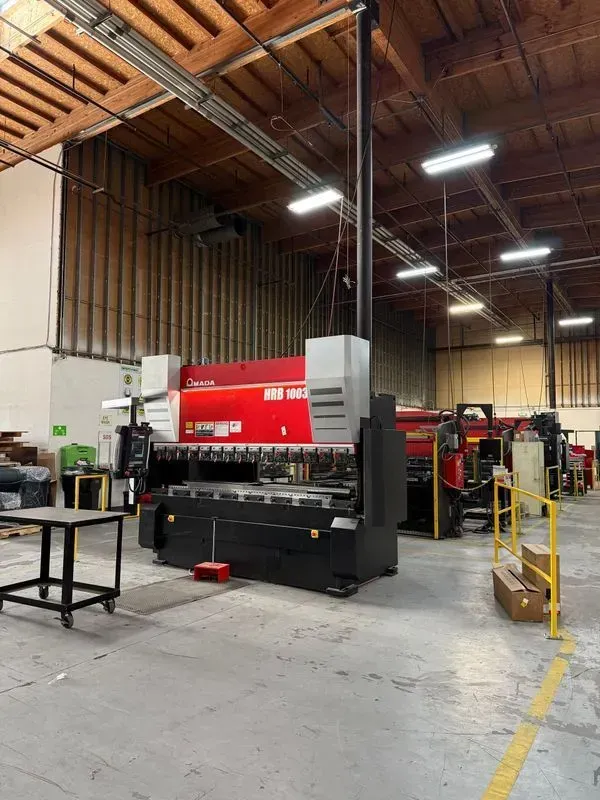 Industrial workshop with a large red-and-black machine, overhead lights, and safety rails in a warehouse.