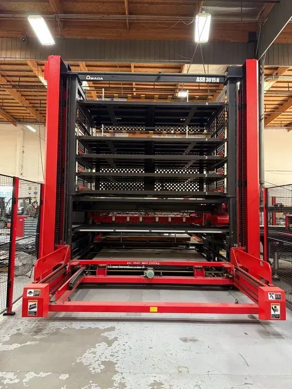 Red industrial lift with stacked metal trays inside a warehouse or workshop