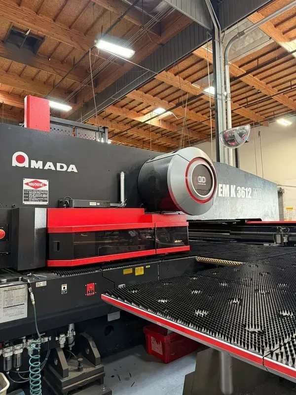 Industrial machine with red and black panels in a factory workshop, under a wooden ceiling.