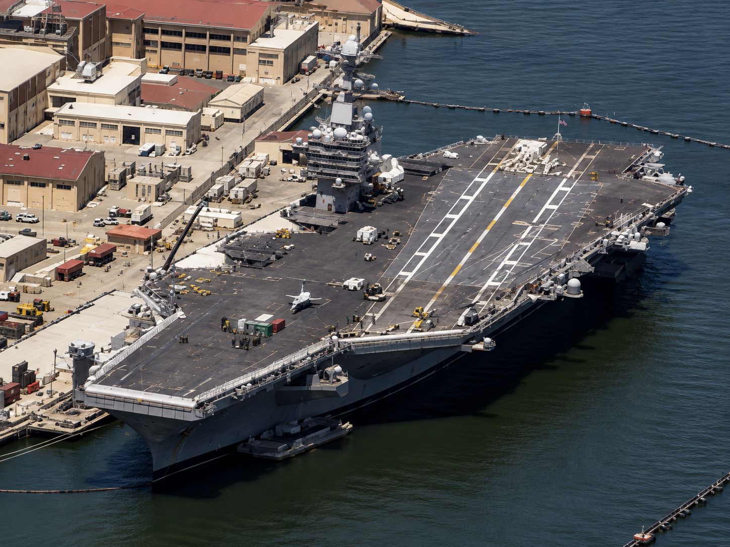 Aircraft carrier docked at a harbor, seen from above with the flight deck and nearby waterfront buildings.
