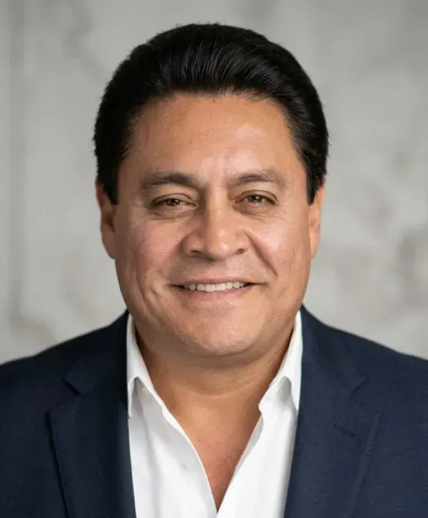 Smiling man in a dark blazer and white shirt against a gray studio background