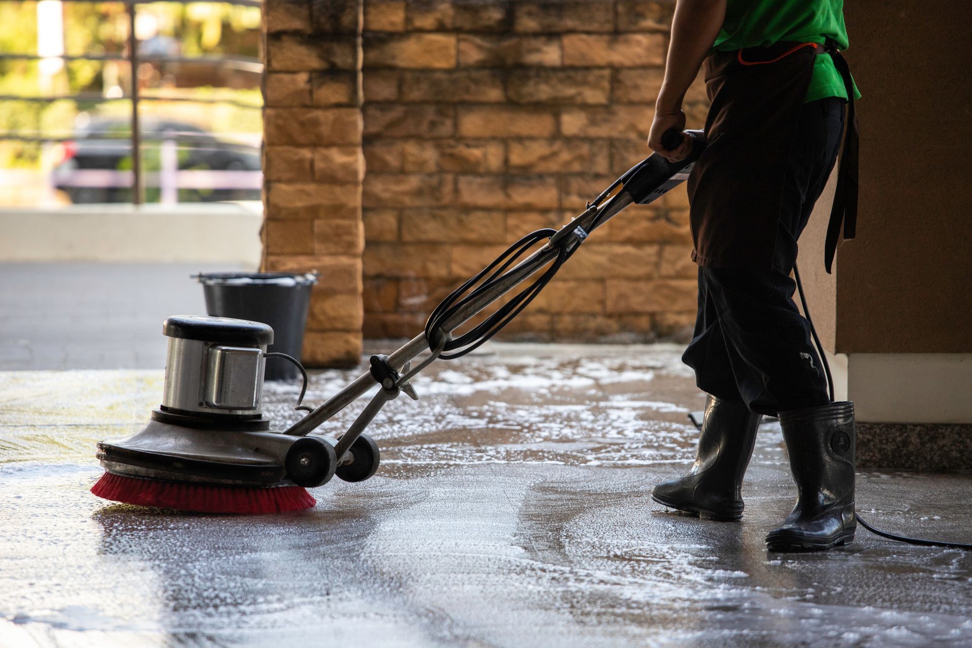 Person using a floor buffer to clean a wet indoor surface near a brick wall