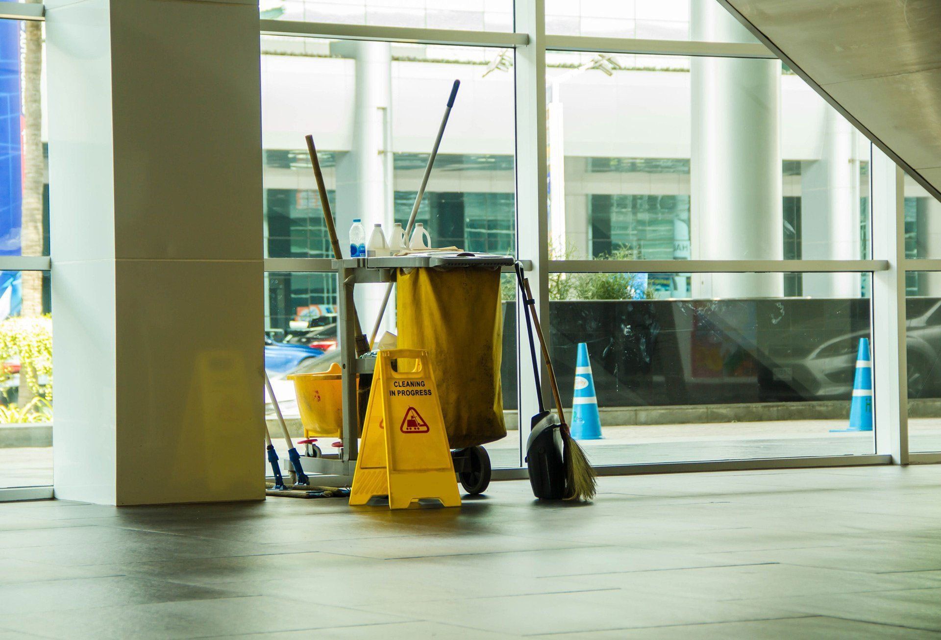 Yellow wet-floor sign and cleaning cart in a glass-walled lobby or terminal entrance Yellow wet-floor sign and cleaning cart in a glass-walled lobby or terminal entrance