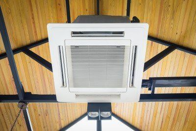 White ceiling air conditioner with open vents mounted on a wooden ceiling. White ceiling air conditioner with open vents mounted on a wooden ceiling.