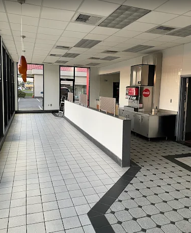 Empty fast-food restaurant interior with white tile floor, counter, and red signage near the entrance Empty fast-food restaurant interior with white tile floor, counter, and red signage near the entrance
