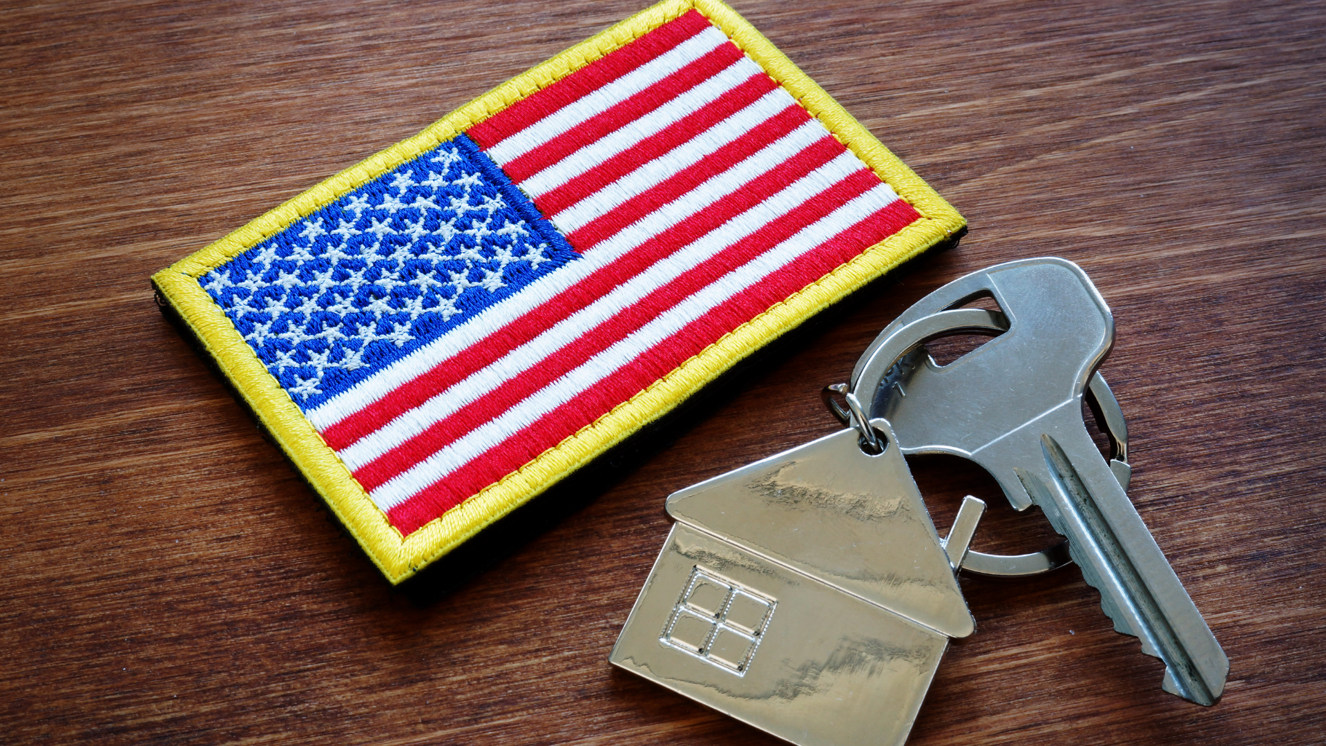 U.S. flag patch beside a key with a house-shaped keychain on a wooden surface